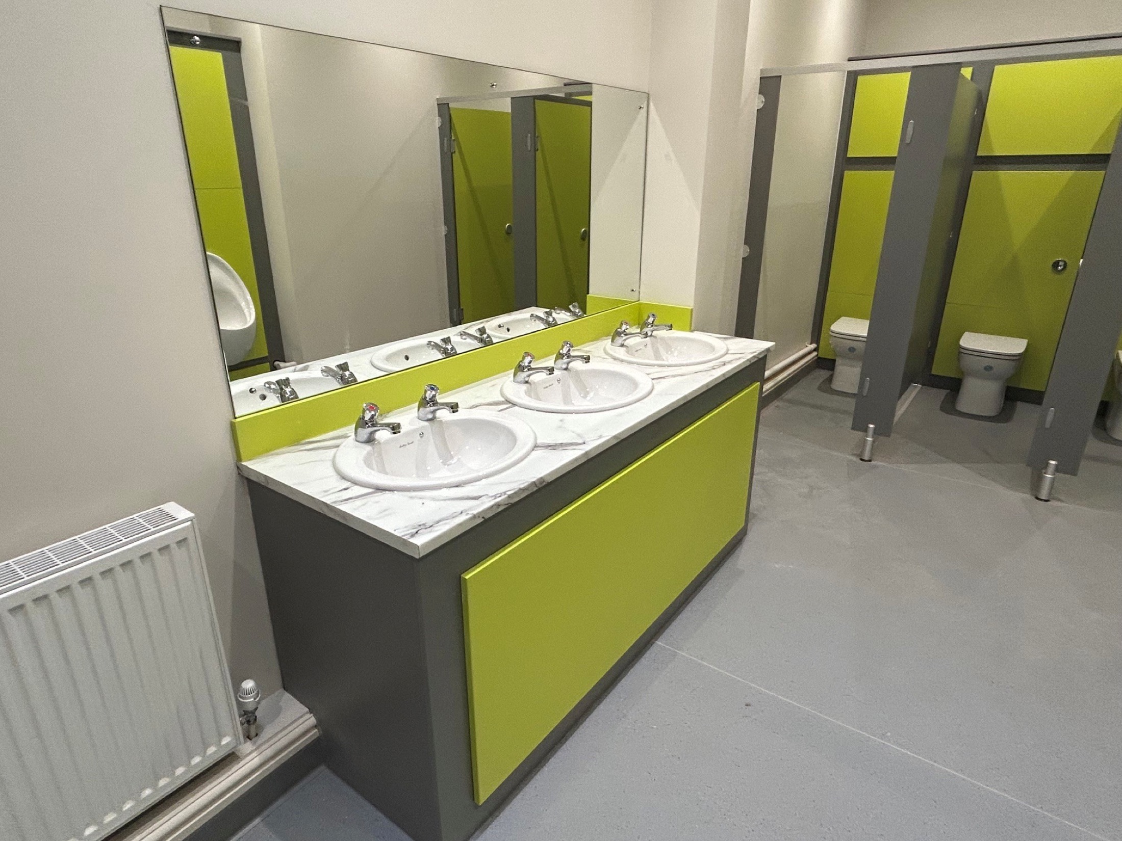 School washroom with grey safety flooring and green cubicle panels